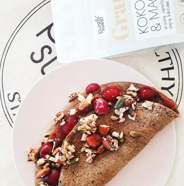 Pfannkuchen mit Kirschen und Pure&Sweet Koko & Mac granola auf einem rosa Teller, daneben die Produktverpackung.